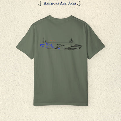 Moss Comfort Colors 1717 water ski shirt shown from the back, featuring minimalist line art of a ski boat pulling a slalom water skier across calm lake water at sunrise with pine trees and blue spray.