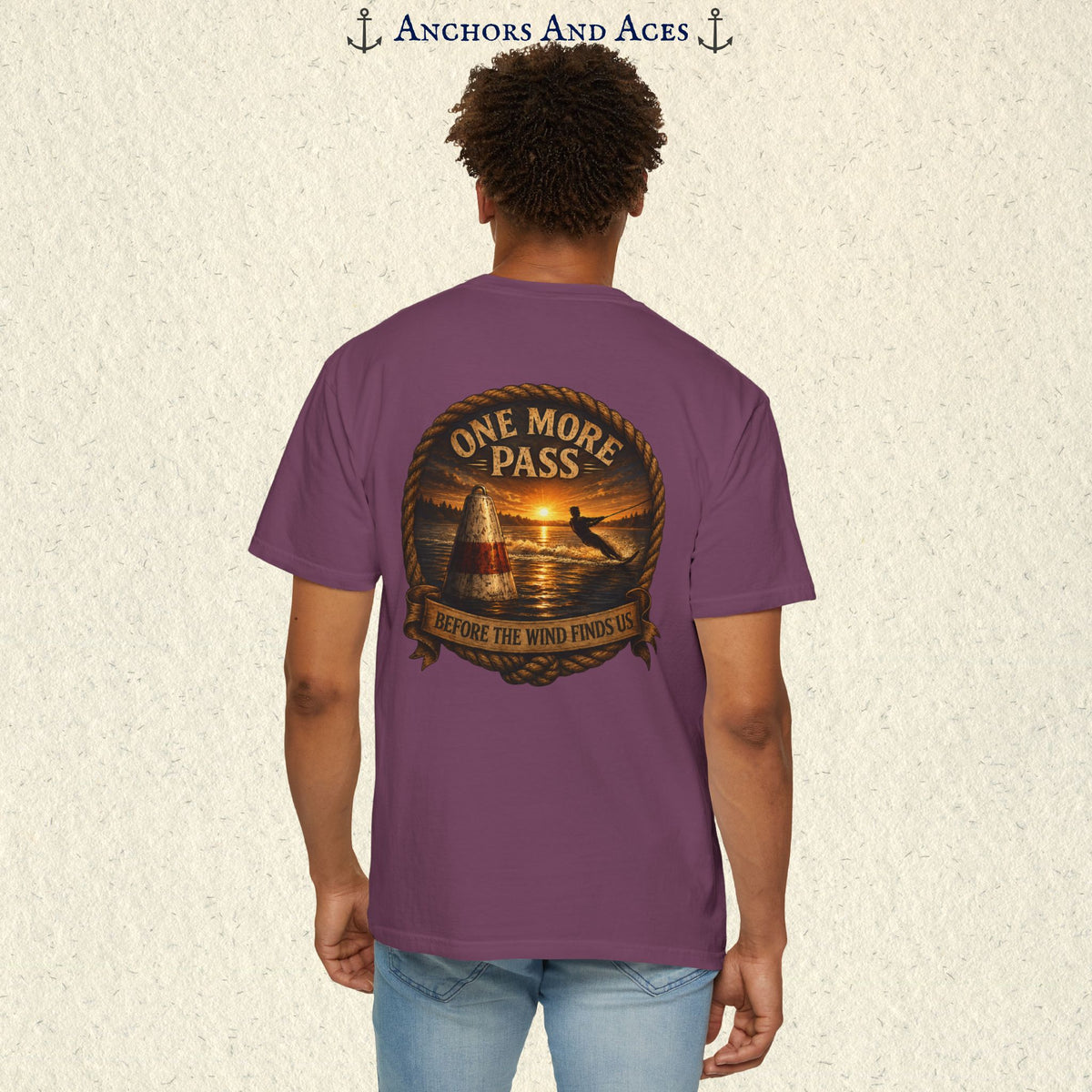 Model wearing a Berry purple vintage slalom water ski T-shirt, back view, with sunrise lake artwork featuring a slalom buoy, water skier, rope border, and One More Pass text.