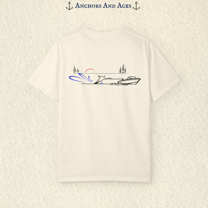 Ivory Comfort Colors 1717 water ski shirt shown from the back, featuring minimalist line art of a ski boat pulling a slalom water skier across calm lake water at sunrise with pine trees and blue spray.