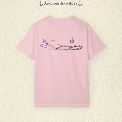 Blossom Comfort Colors 1717 water ski shirt shown from the back, featuring minimalist line art of a ski boat pulling a slalom water skier across calm lake water at sunrise with pine trees and blue spray.