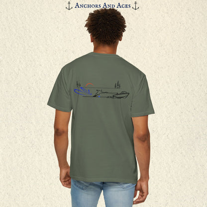 Model wearing a Moss Comfort Colors 1717 water ski t-shirt from the back, featuring minimalist line art of a ski boat pulling a slalom water skier at sunrise with pine trees and blue spray.