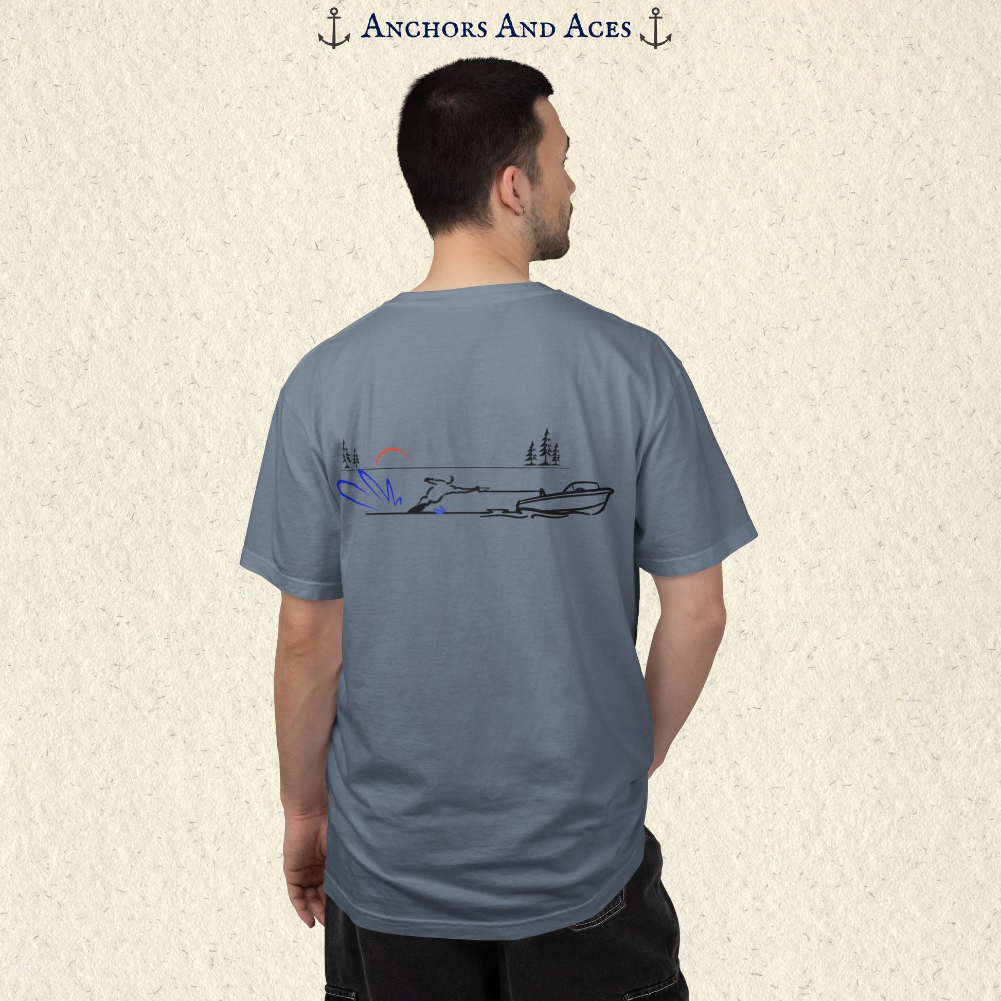 Model wearing a Blue Jean Comfort Colors 1717 water ski t-shirt from the back, featuring minimalist line art of a ski boat pulling a slalom water skier at sunrise with pine trees and blue spray.