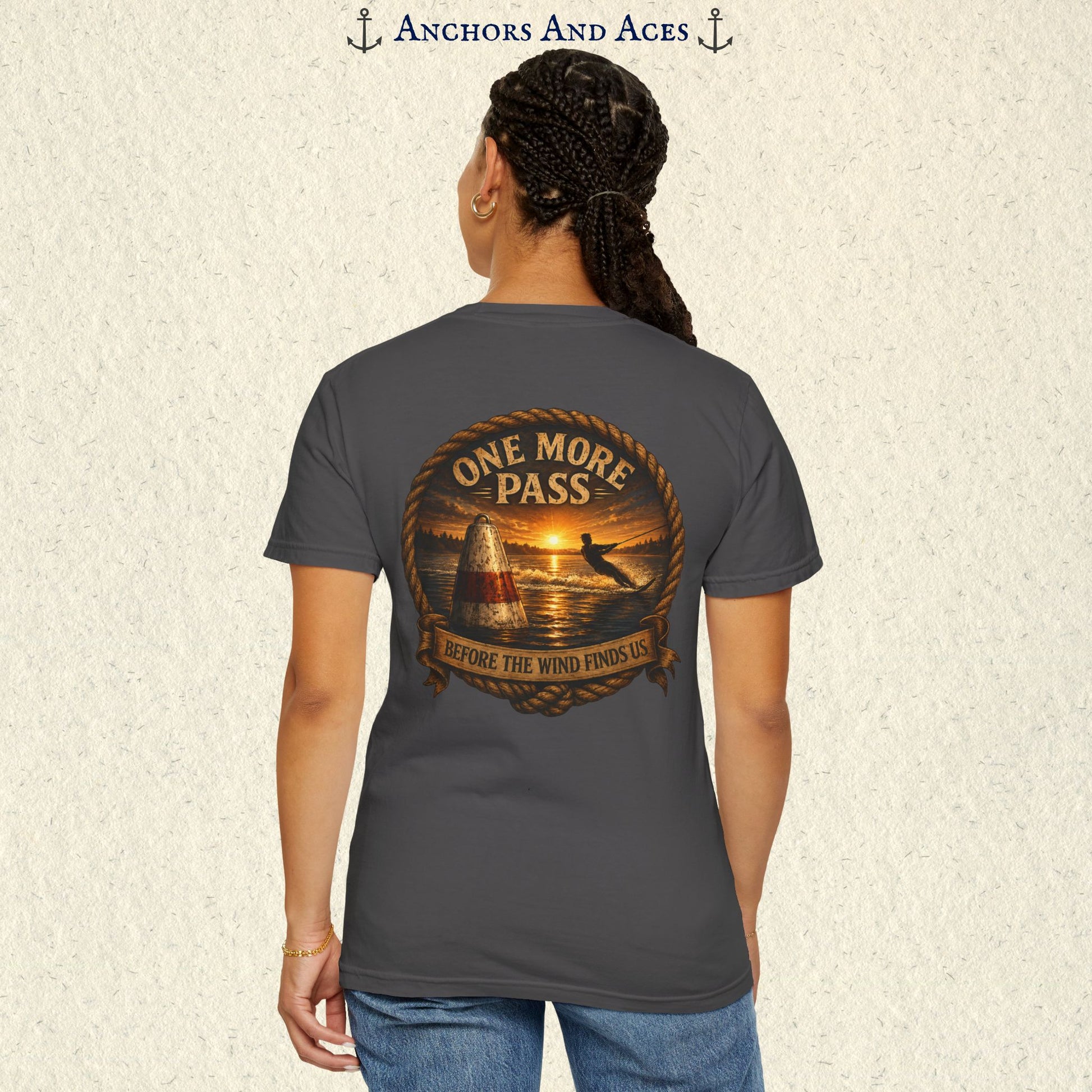 Model wearing a Graphite gray vintage slalom water ski T-shirt, back view, with sunrise lake artwork featuring a slalom buoy, water skier, rope border, and One More Pass text.