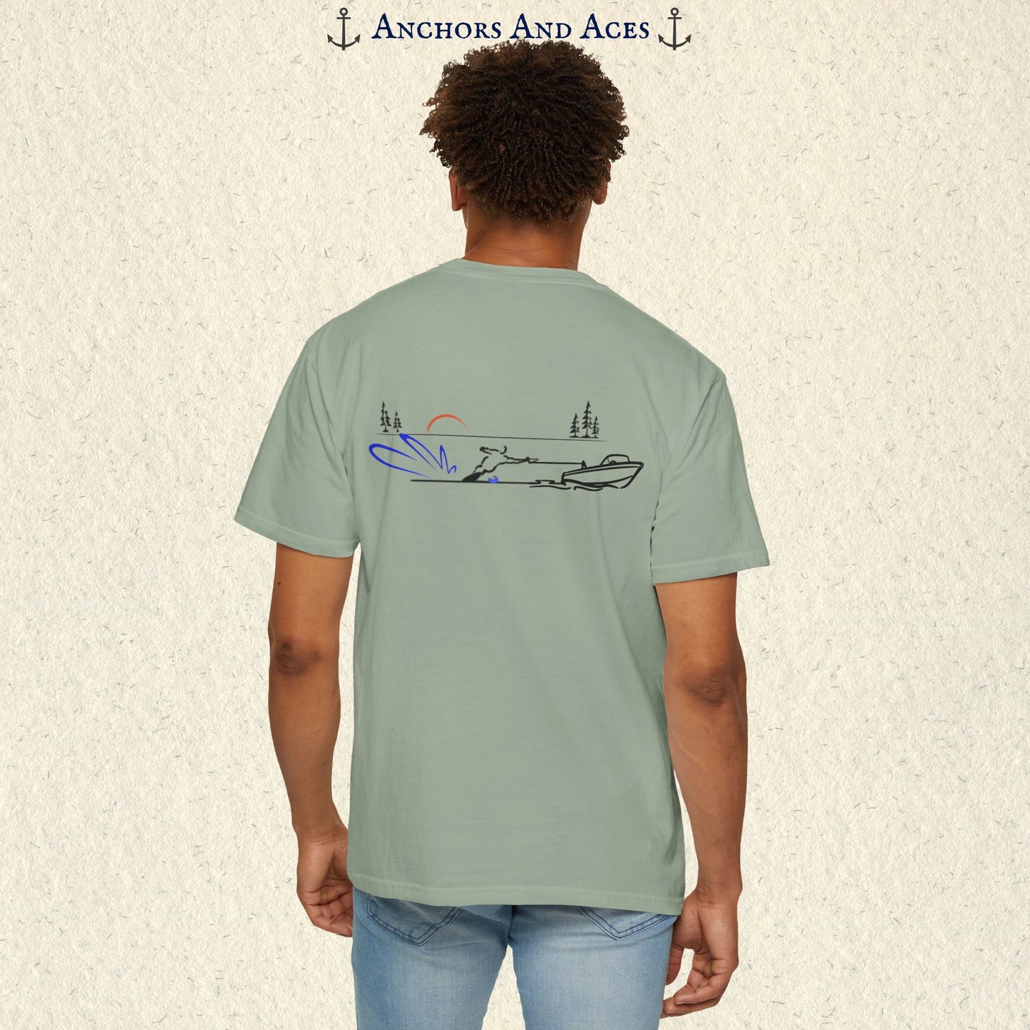 Model wearing a Bay Comfort Colors 1717 water ski t-shirt from the back, featuring minimalist line art of a ski boat pulling a slalom water skier at sunrise with pine trees and blue spray.