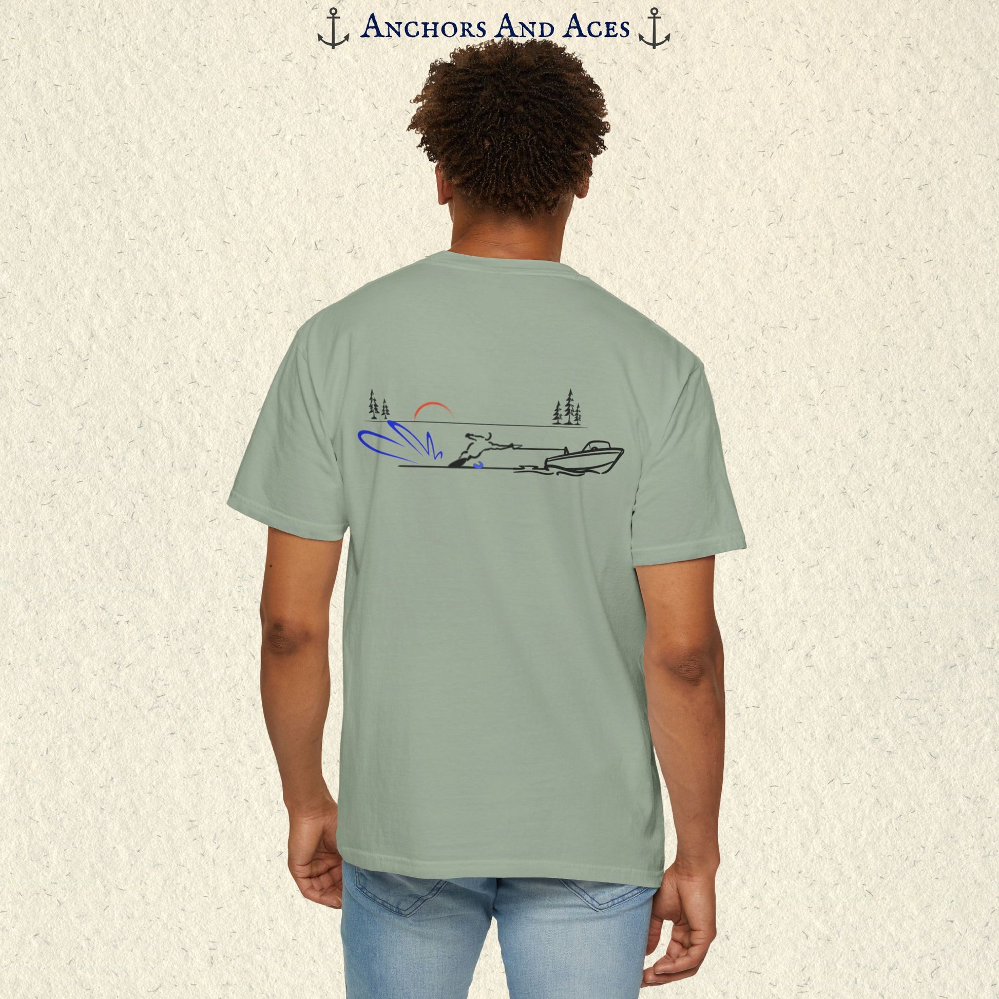 Model wearing a Bay Comfort Colors 1717 water ski t-shirt from the back, featuring minimalist line art of a ski boat pulling a slalom water skier at sunrise with pine trees and blue spray.