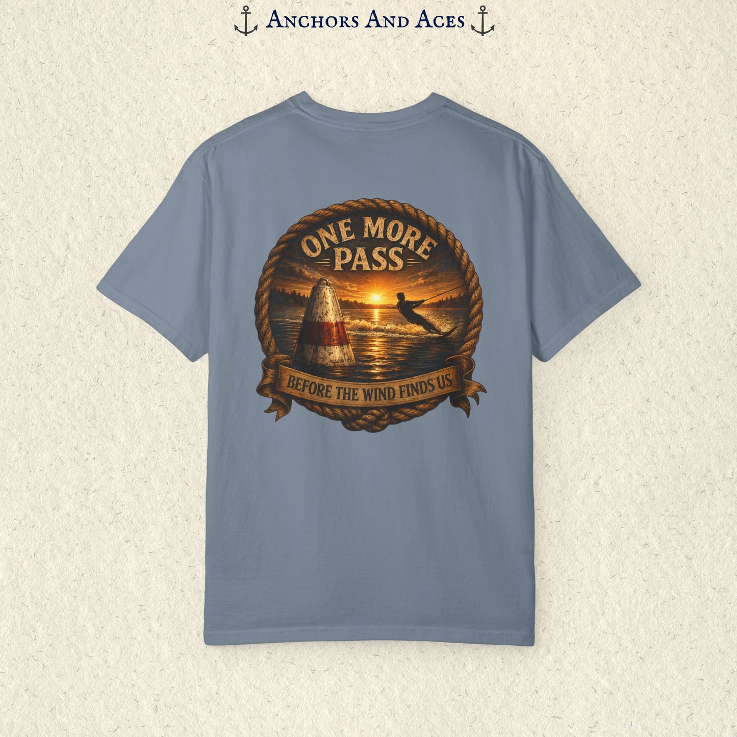 Blue Jean blue vintage slalom water ski T-shirt shown from the back with a sunrise lake graphic featuring a slalom buoy, water skier, rope border, and the text One More Pass and Before the Wind Finds Us.
