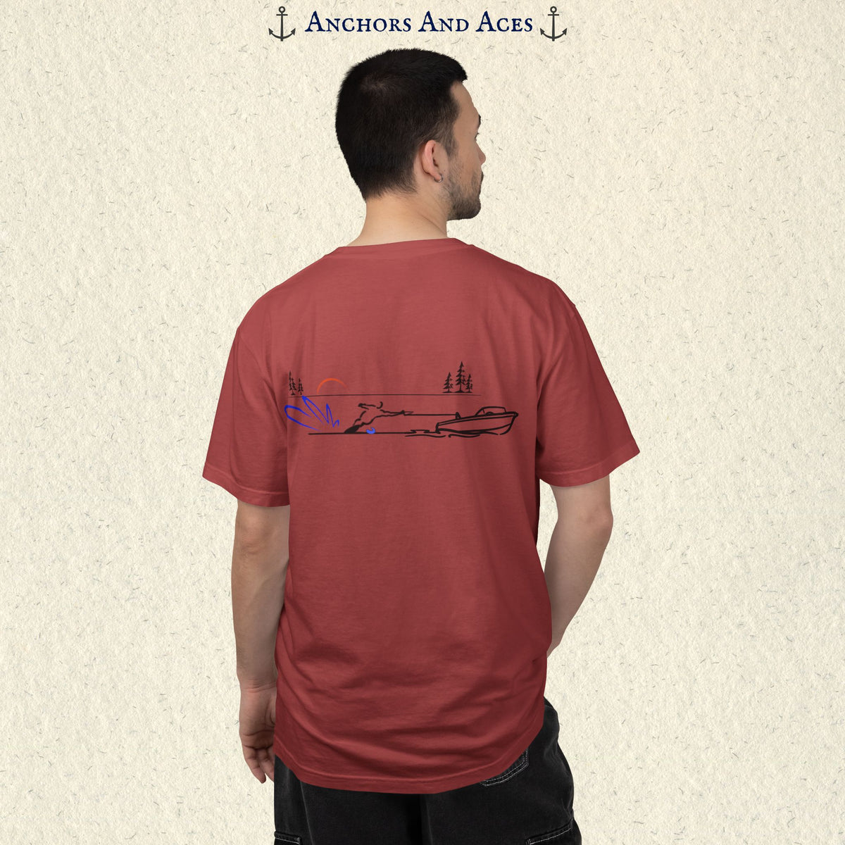 Model wearing a Crimson Comfort Colors 1717 water ski t-shirt from the back, featuring minimalist line art of a ski boat pulling a slalom water skier at sunrise with pine trees and blue spray.