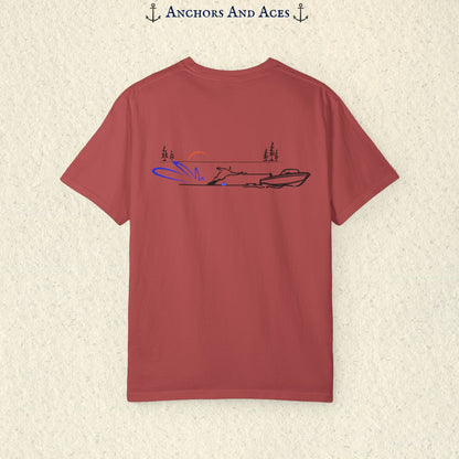 Crimson Comfort Colors 1717 water ski shirt shown from the back, featuring minimalist line art of a ski boat pulling a slalom water skier across calm lake water at sunrise with pine trees and blue spray.