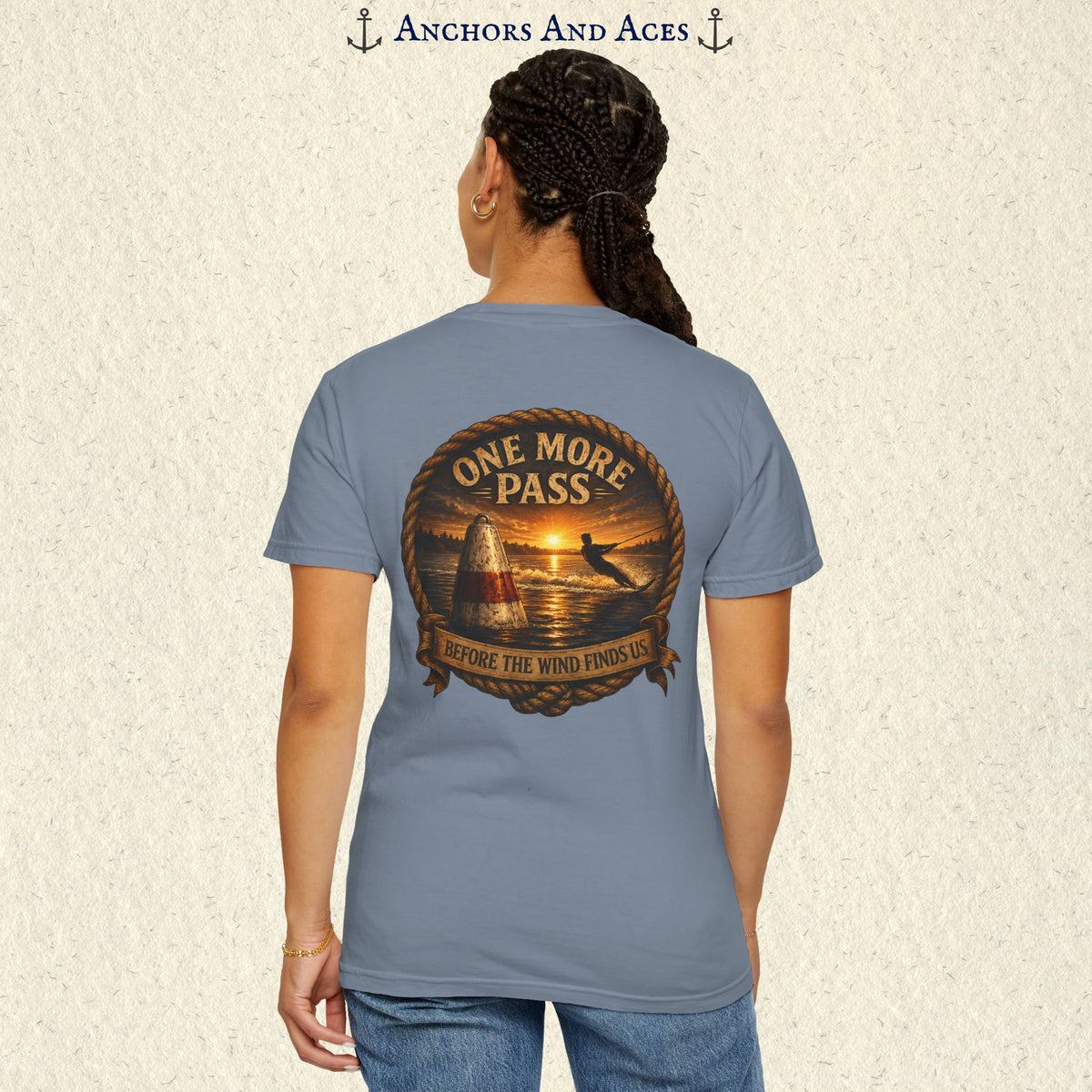 Model wearing a Blue Jean blue vintage slalom water ski T-shirt, back view, with sunrise lake artwork featuring a slalom buoy, water skier, rope border, and One More Pass text.