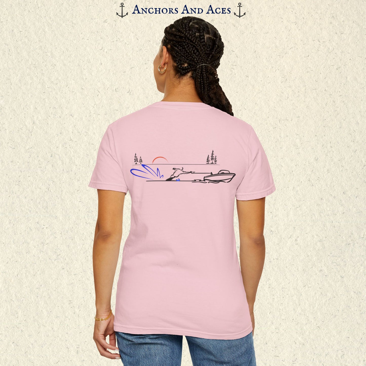 Model wearing a Blossom Comfort Colors 1717 water ski t-shirt from the back, featuring minimalist line art of a ski boat pulling a slalom water skier at sunrise with pine trees and blue spray.