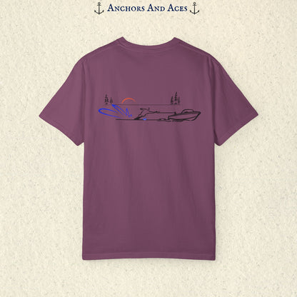 Brick Comfort Colors 1717 water ski shirt shown from the back, featuring minimalist line art of a ski boat pulling a slalom water skier across calm lake water at sunrise with pine trees and blue spray.