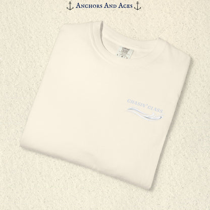 Folded Ivory Comfort Colors 1717 t-shirt showing the front left-chest Chasin' Glass logo, featuring white lettering above a stylized water-splash graphic.