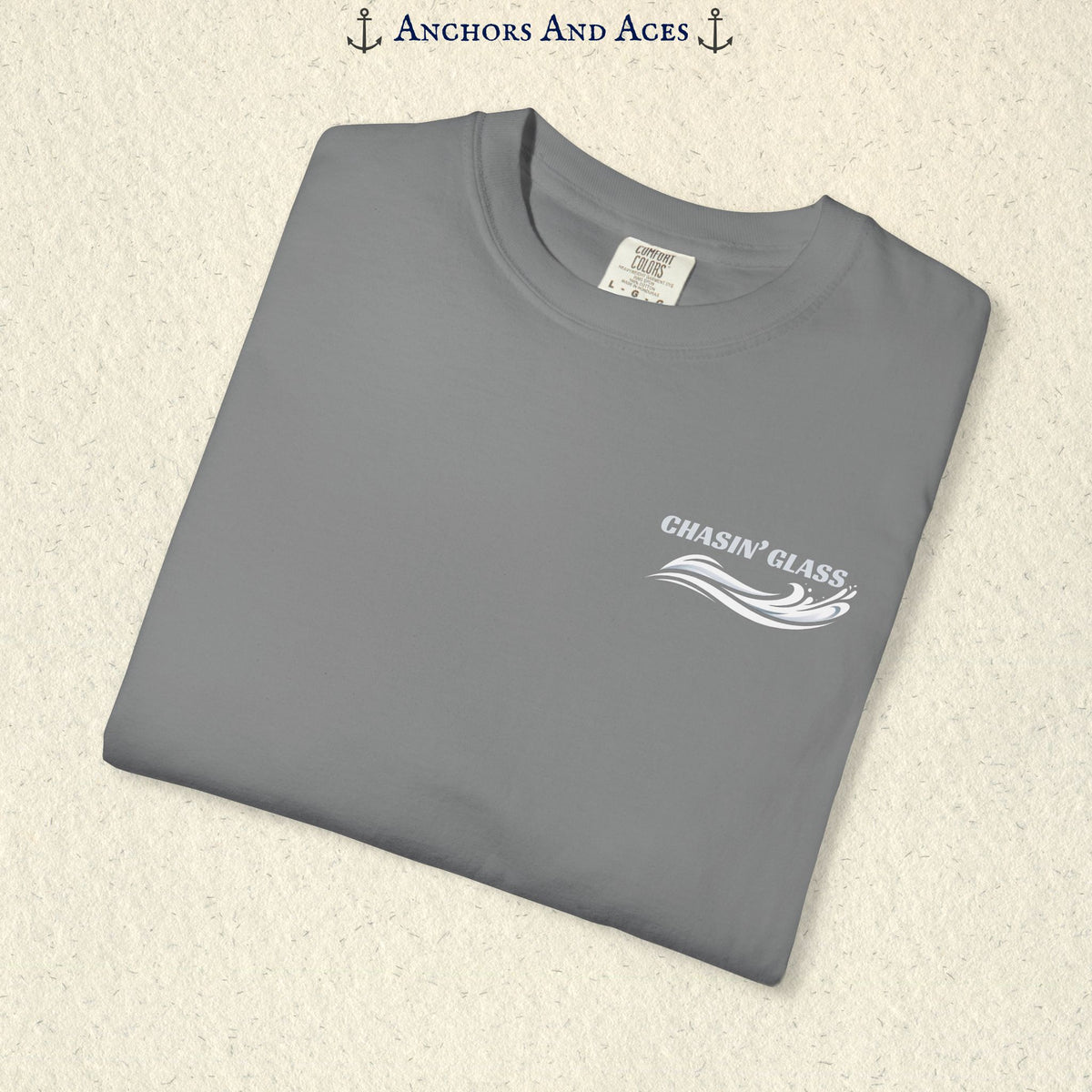 Folded Grey Comfort Colors 1717 t-shirt showing the front left-chest Chasin' Glass logo, featuring white lettering above a stylized water-splash graphic.