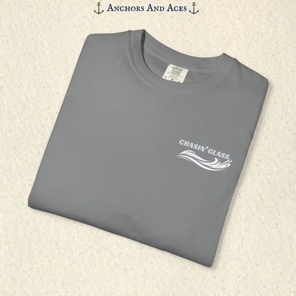 Folded Grey Comfort Colors 1717 t-shirt showing the front left-chest Chasin' Glass logo, featuring white lettering above a stylized water-splash graphic.